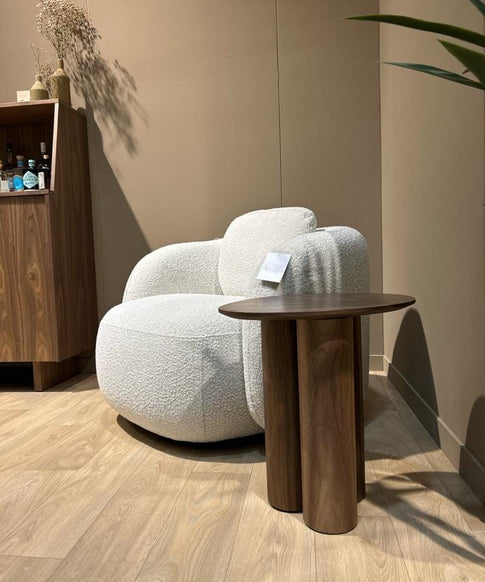 Une table d'appoint en bois de noyer près d'un fauteuil bouclette