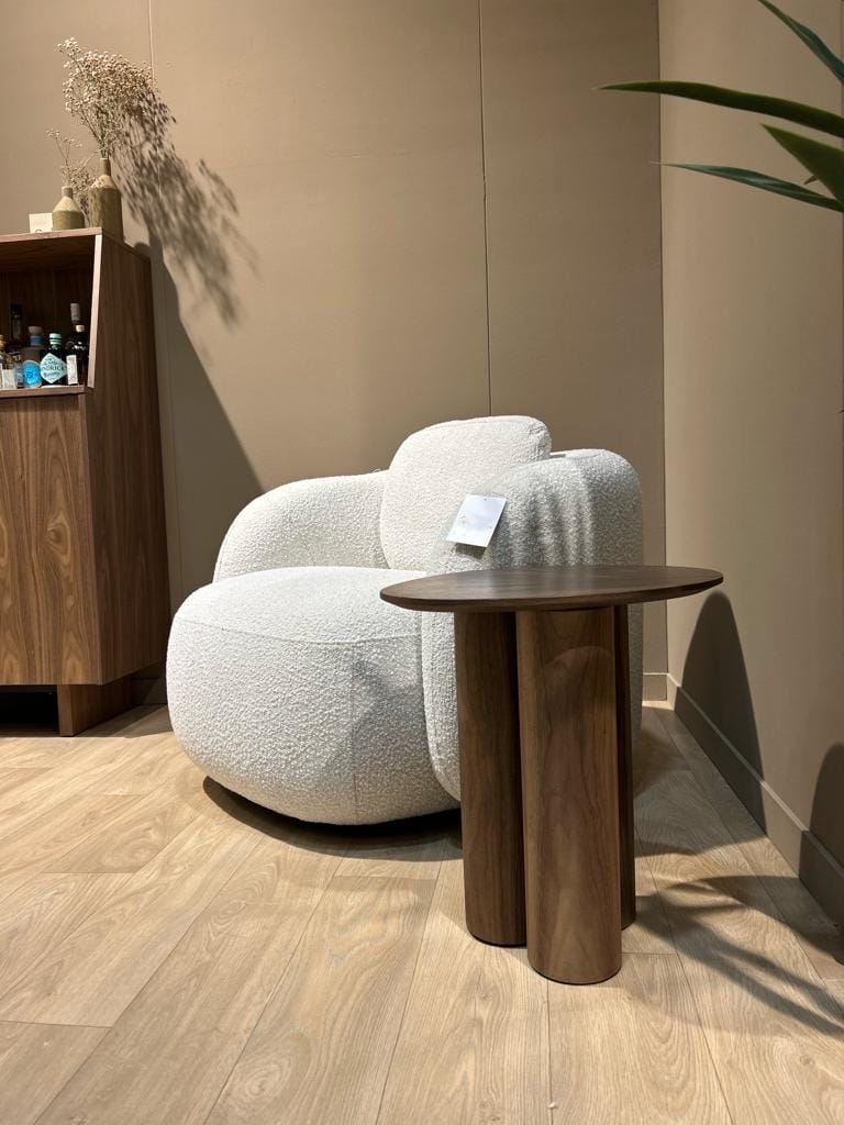 Une table d'appoint en bois de noyer près d'un fauteuil bouclette